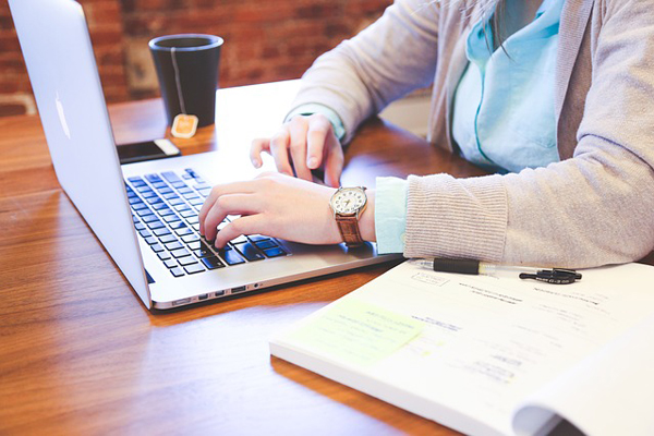 Fotografía de una mujer sentada frente a una laptop con un libro al lado. 