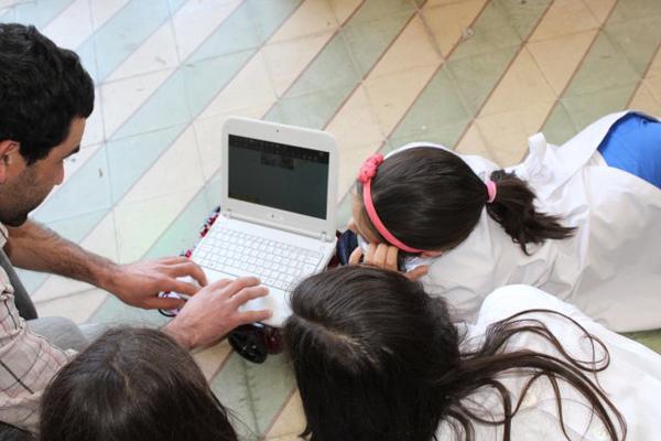 Fotografía de un docente y tres alumnos mirando una laptop.