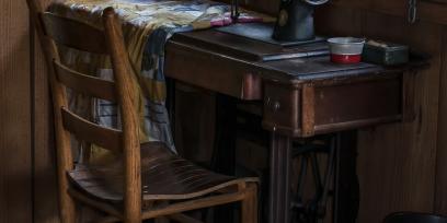 Imagen que muestra una máquina de coser antigua, sobre una mesa y junto a una silla