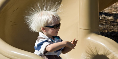 Niño bajando por un tobogán de plástico con sus cabellos electrizados, tiene los cabellos parados, repelidos por la fuerza eléctrica entre cargas de igual signo entre ellos.