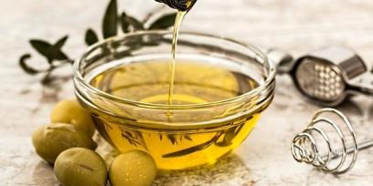 Imagen de recipiente con aceite de oliva y unas aceitunas alrededor.