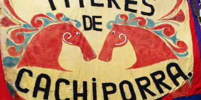 Bandera en tonos rojos y azules con las imágenes de las cabezas de dos caballos y el nombre de la compañía titiritera: "Títeres de Cachiporra" 