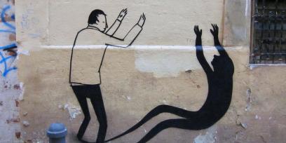 Imagen de un graffiti en un muro de un niño jugando con su sombra.