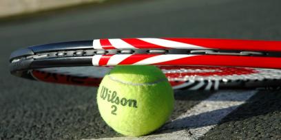 Raqueta sobre pelota de tenis apoyada en el suelo