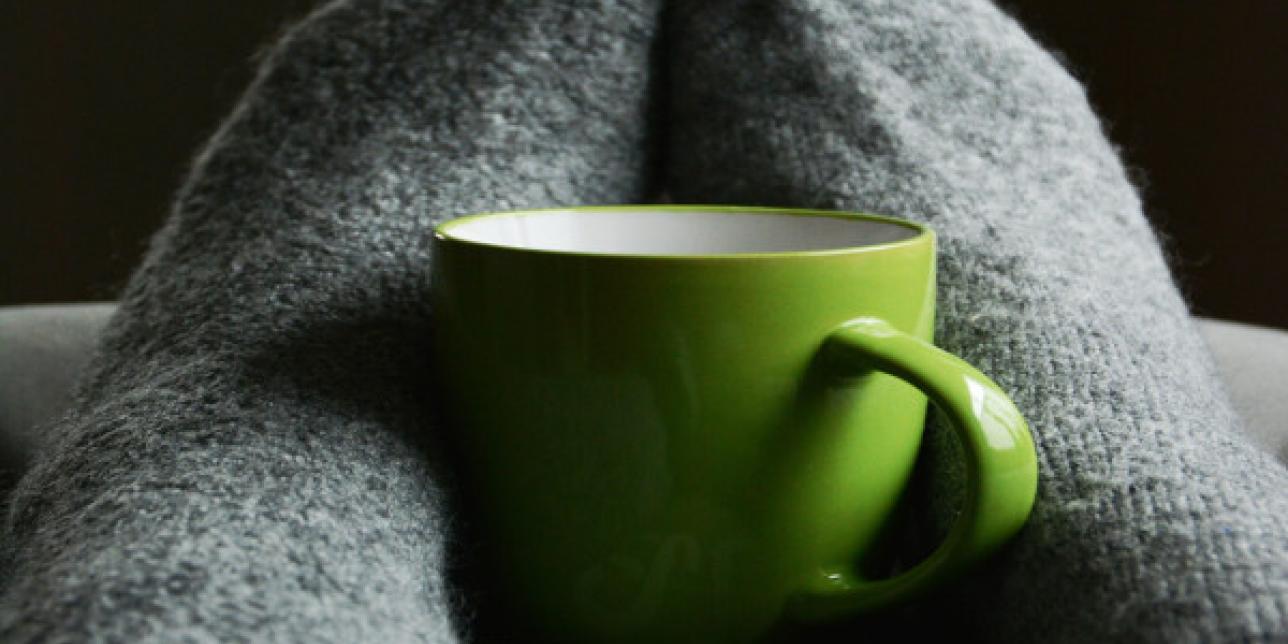 Pies con medias grises abrazando una taza verde.