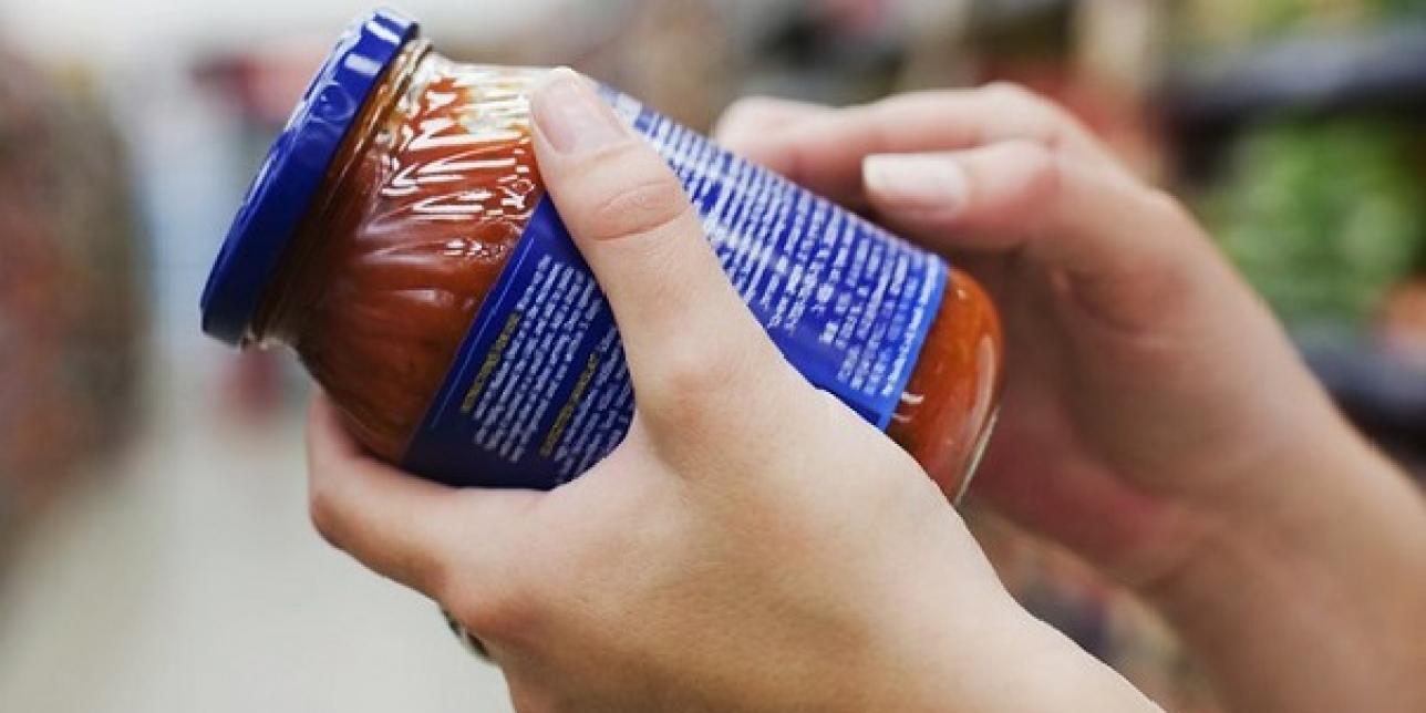 Imagen de persona en un supermercado mirando la etiqueta de un frasco de alimento