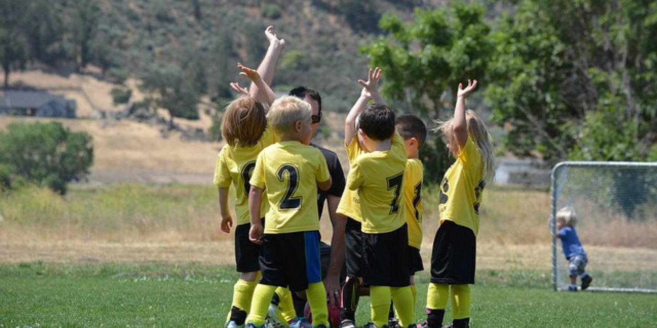 Niños y niñas rodeando al profesor vestidos con indumentaria de un equipo deportivo verde y amarillo