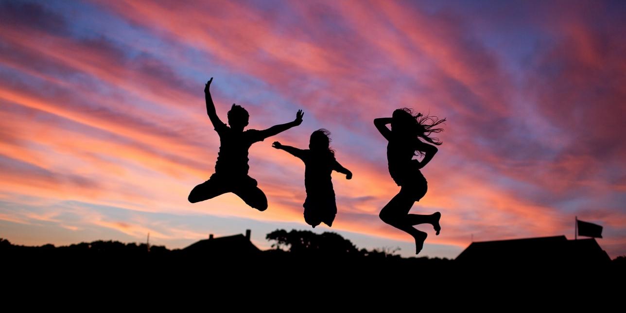 Tres jóvenes saltando, la imagen captura un instante de la fase de vuelo, al atardecer, a contraluz