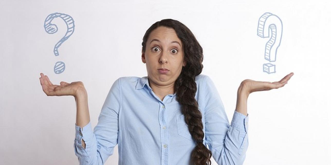 Joven mujer con gesto de dudas, las manos a los dados y los hombros levantados. Sobre cada mano hay un signo de pregunta. 