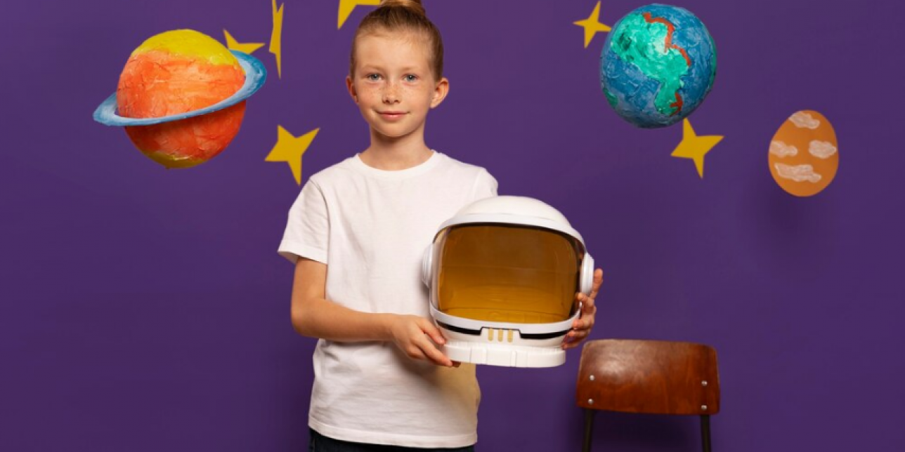 niña con casco de astronauta en la mano y fondo de planetas