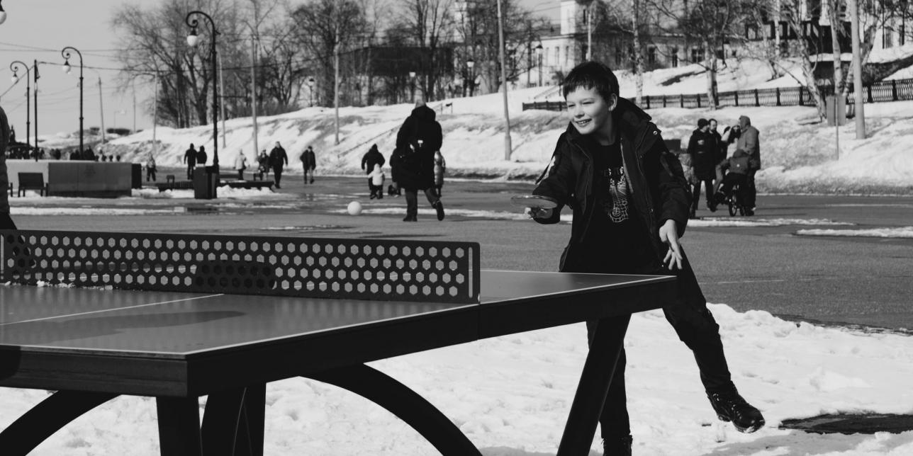 niño jugando tenis de mesa con una mesa de ping pong en un espacio publico