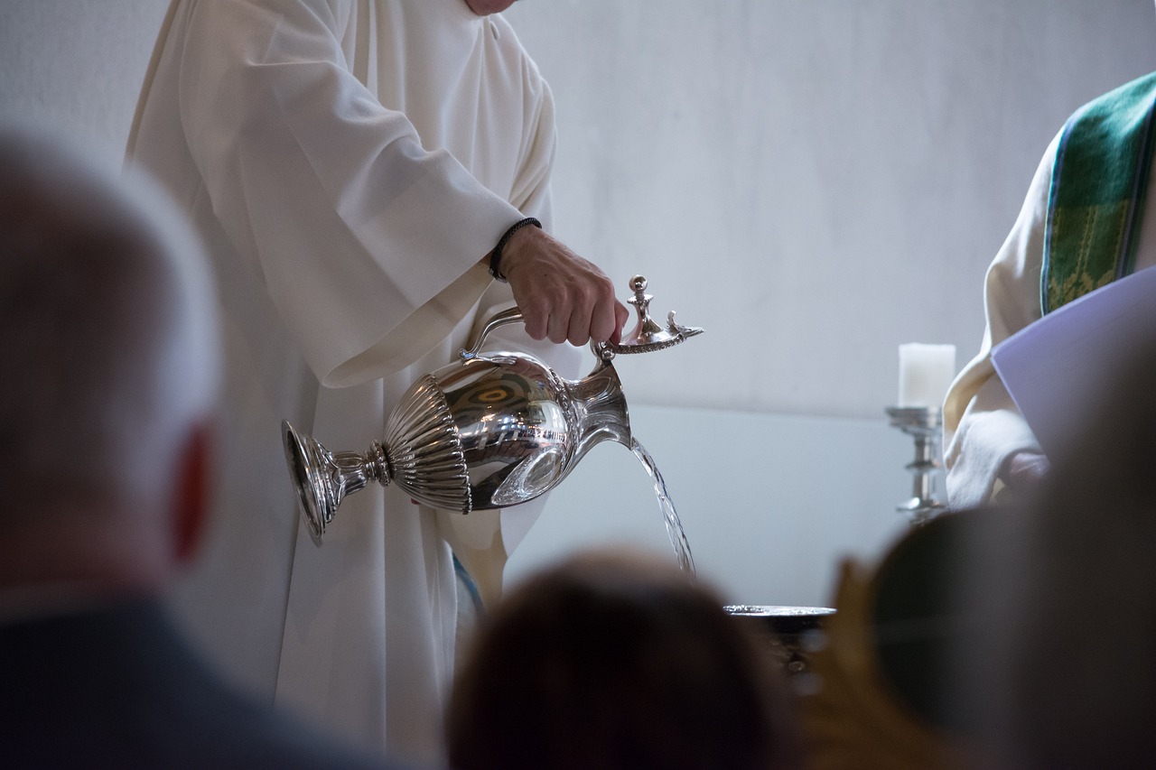 Sacerdote usando jarra con agua en una pila bautismal