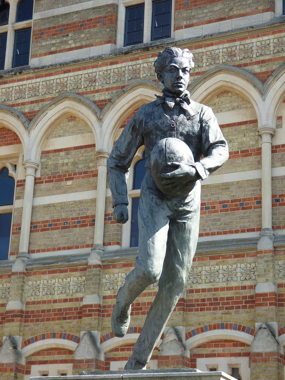 William Webb Ellis aparece corriendo con el balón. Se encuentra en la localidad de Rugby.