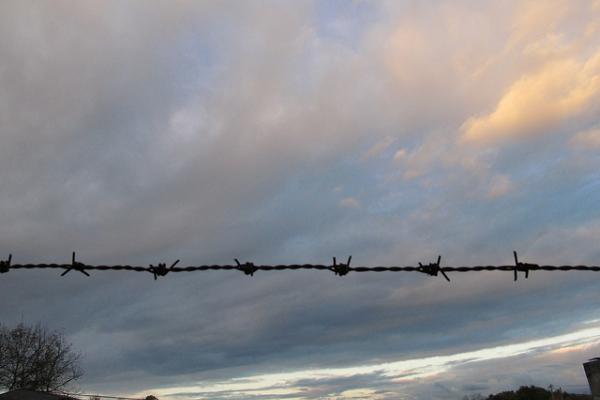 Fotografía de un atardecer atravesado por un alambre de púa en primer plano.