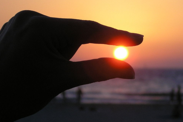 Dedos índice y pulgar "sosteniendo" al sol en el atardecer.