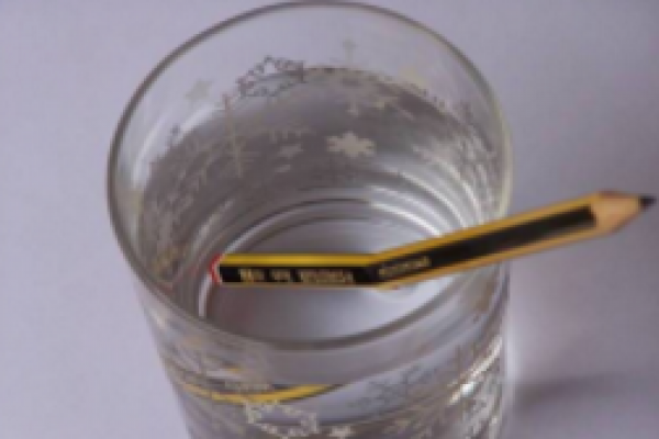 Vaso con agua y un lápiz amarillo y negro. La mitad del lápiz se encuentra sumergido en el agua y la foto es tomada desde arriba. Se observa el fenómeno de refracción.