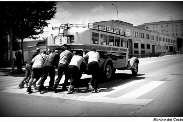 Foto en blanco y negro de un conjunto de personas empujando un ómnibus antiguo.