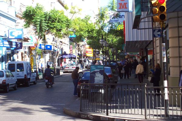 Fotografía de una calle donde se ven autos, motos y peatones. 