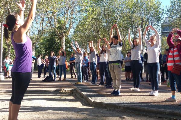 Fotografía de una profesora dirigiendo clase de gimnasia aeróbica en una plaza.