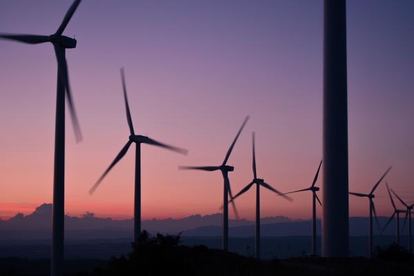 Imagen que muestra varios molinos de viento. De fondo, la luz de un atardecer.