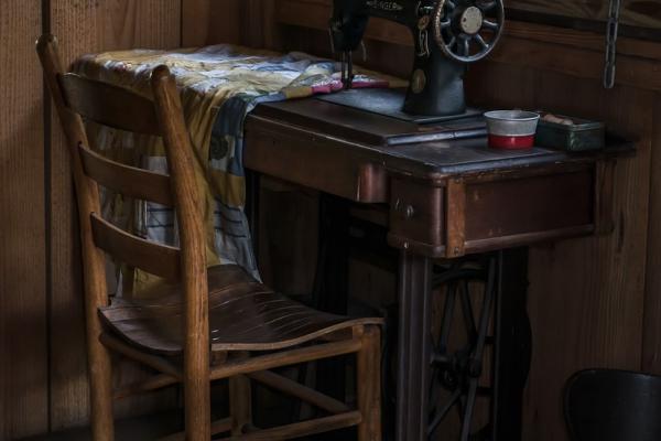 Imagen que muestra una máquina de coser antigua, sobre una mesa y junto a una silla