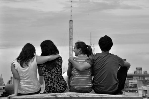 Fotografía de cuatroa dolescentes de espaldas, sentados en un muro. 