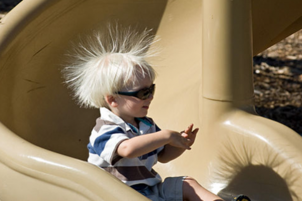 Niño bajando por un tobogán de plástico con sus cabellos electrizados, tiene los cabellos parados, repelidos por la fuerza eléctrica entre cargas de igual signo entre ellos.