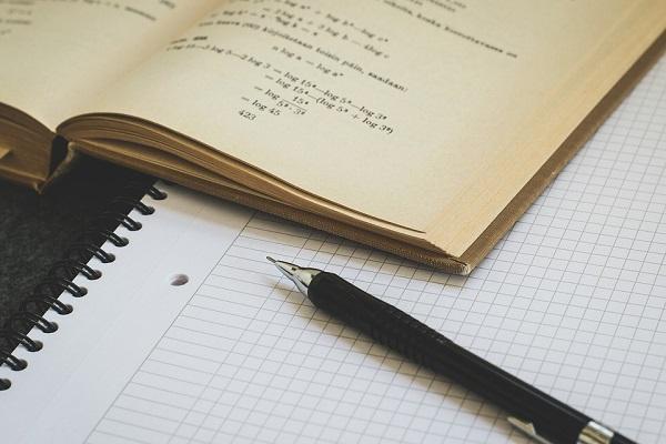 Fotografía de un libro abierto sobre un cuaderno junto a un lápiz