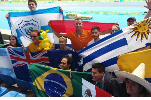 Grupo de personas de diferentes países con sus banderas en tribuna de estadio olímpico.