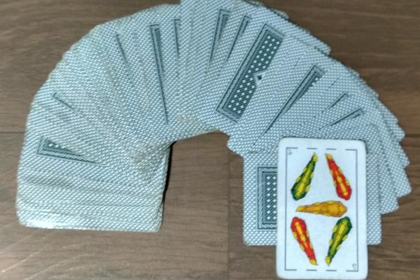 Mazo de naipes con cartas presentadas boca abajo y una dada vuelta en la cual se visualiza un cinco de basto.