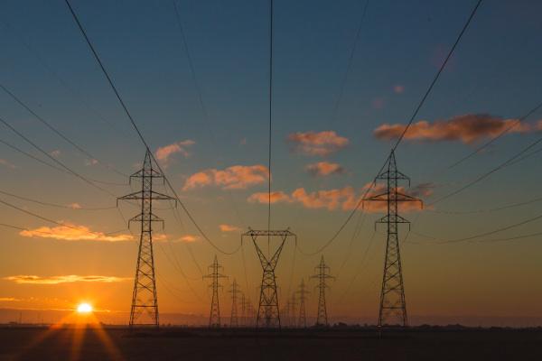 Puesta de sol, en el campo y se ven las torres de alta tensión que sostienen las redes eléctricas.