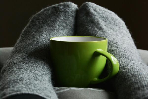 Pies con medias grises abrazando una taza verde.