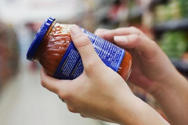 Imagen de persona en un supermercado mirando la etiqueta de un frasco de alimento