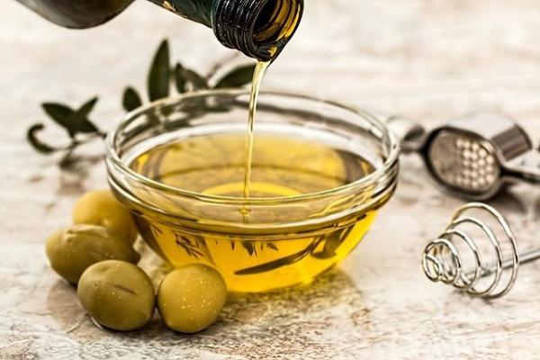 Imagen de recipiente con aceite de oliva y unas aceitunas alrededor.