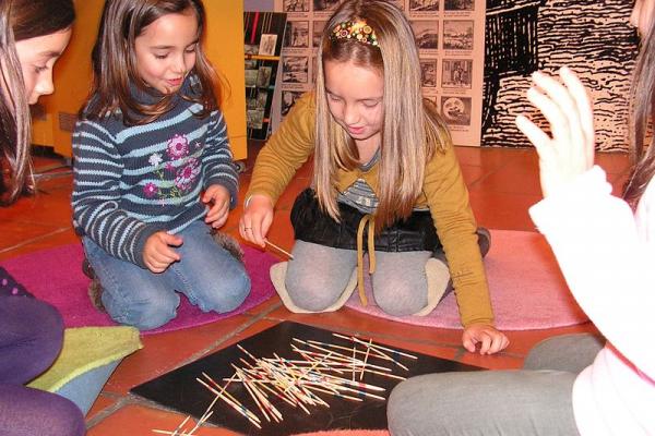 Cuatro niñas jugando a los palitos chinos en el piso.
