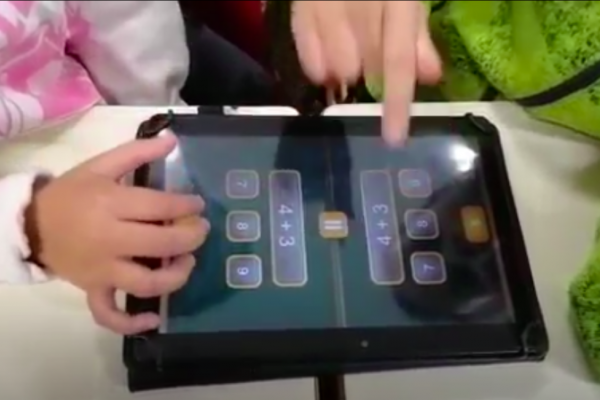 dupla de niños enfrentados con una tablet con la aplicación Math Duel sumando dígitos