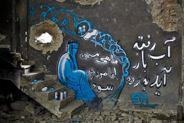 Fotografía de un muro graffiteado, se aprecia una mujer con su burka en tonos de azul y un texto en árabe. Aparecen los aerosoles usados, una escalera de cemento
