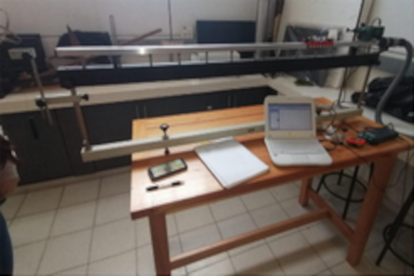 La imagen muestra el diseño experimental de una de las actividades compartidas en el artículo. Muestra una mesa sobre la que se encuentra una computadora conectada a una interfase Vernier, un riel con un carrito que presenta un dispositivo para disminuir la fricción entre las superficies.