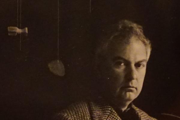 Imagen de Alexander Calder en tonos sepia junto a un móvil.