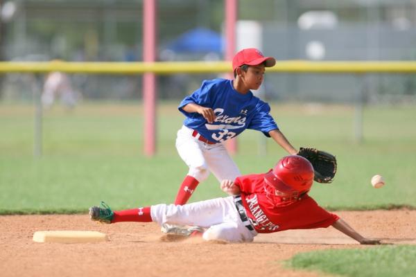 niño (corredor), barriendose para llegar a tocar una base, antes que la pelota llegue al niño en defensa