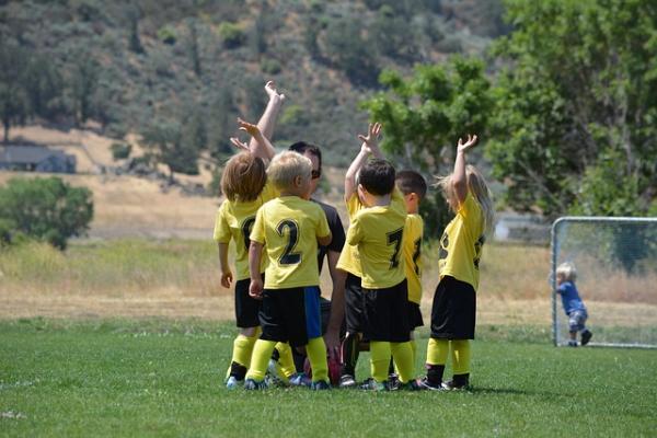 Niños y niñas rodeando al profesor vestidos con indumentaria de un equipo deportivo verde y amarillo