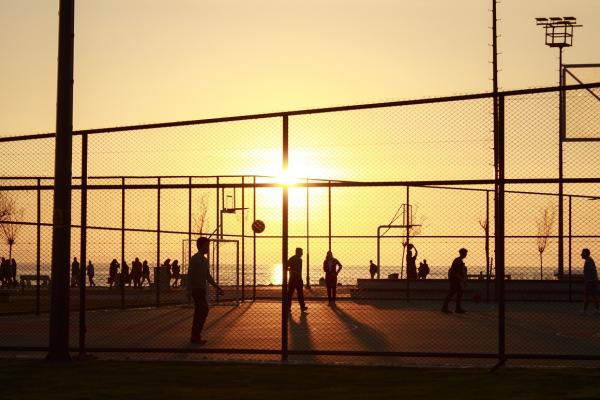 Imagen decorativa con un plano general de una cancha de basketball a contra luz del atardecer