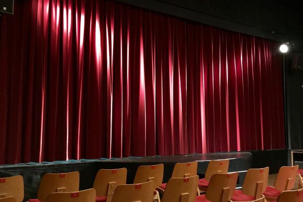 Cortina roja en sala de teatro iluminada con dos focos de luz blanca. 