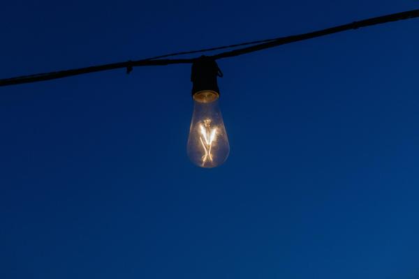 Lamparilla eléctrica encendida, conectada con un cable a ambos lados, a la que se le puede ver el filamento. Fondo azul oscuro. 