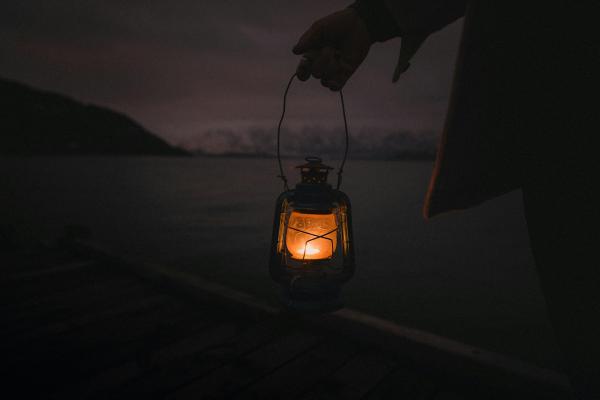 Farol encendido colgando de una mano en espacio abierto nocturno