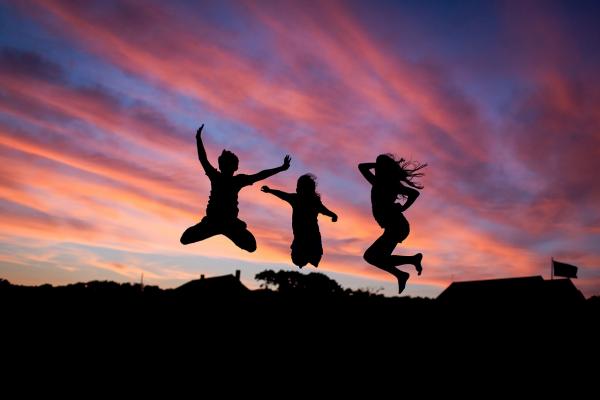 Tres jóvenes saltando, la imagen captura un instante de la fase de vuelo, al atardecer, a contraluz