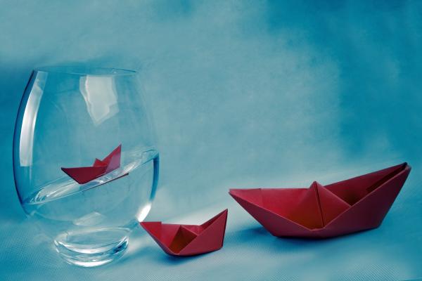 Vaso de vidrio con agua y tres barcos de papel plegado.