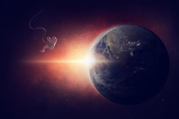 Representación del planeta Tierra en el espacio, la luz del Sol se asoma por la izquierda del planeta. Un astronauta se ve también del lado de la izquierda, flotando. 