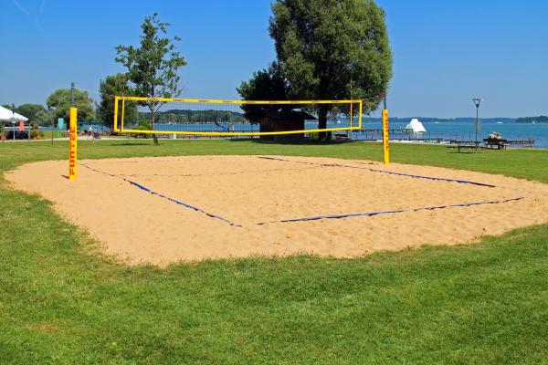 Cancha de voleibol al aire libre, con una superficie de arena suave en la zona de juego y rodeada de césped verde. La red está colocada en el centro, dividiendo el campo en dos mitades simétricas. El entorno natural crea un ambiente relajado, ideal para actividades deportivas al aire libre.
