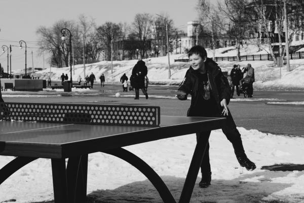 niño jugando tenis de mesa con una mesa de ping pong en un espacio publico